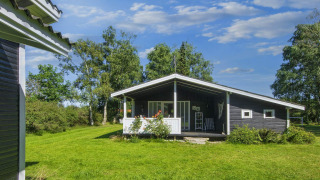 Foto van een 6-persoons vakantiehuis in Glesborg met veranda, tuin en groene bomen rondom.