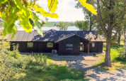 Maison de vacances à Millinge, Danemark, entourée d’arbres, lac en arrière-plan, atmosphère estivale.