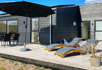 Terrasse ensoleillée d'une maison de vacances à Ansager, Danemark, avec transats, parasol et coin repas.
