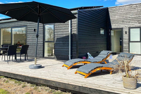 Zonnig terras bij vakantiewoning in Ansager, Denemarken, met ligbedden, parasol en eethoek.
