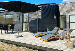 Terrazza soleggiata di una casa vacanze ad Ansager, Danimarca, con lettini, ombrellone e zona pranzo.