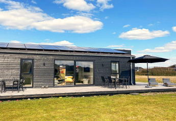 Vue extérieure d'un pavillon de vacances en bois moderne avec terrasse, chaises longues et parasol à Ansager, Danemark.