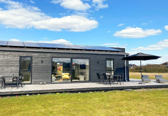 Buitenaanzicht van een modern houten vakantiehuis met ligstoelen, parasol en terras in Ansager, Denemarken.