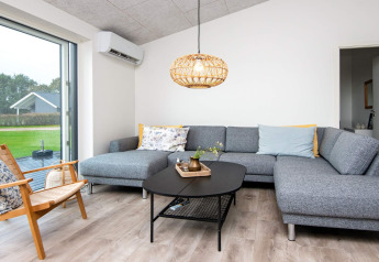 Salón moderno en casa de vacaciones para 8 personas en Ansager, Dinamarca, con sofá gris y ventanal.