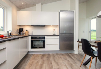 Cuisine moderne avec armoires blanches, grand réfrigérateur et coin repas dans une maison de vacances à Ansager.
