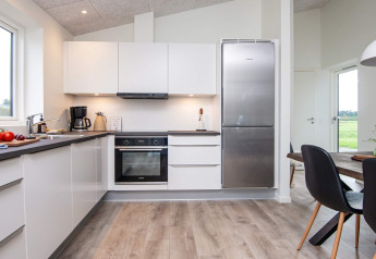 Cocina moderna con armarios blancos, nevera grande y comedor en casa de vacaciones para 8 personas en Ansager.