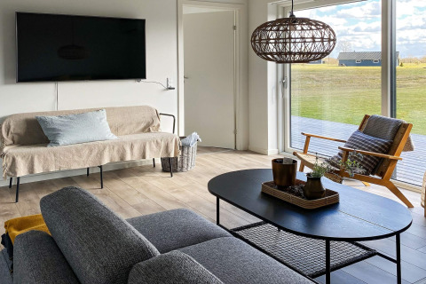 Salón luminoso y moderno en casa de vacaciones en Dinamarca con ventanales, sofá y vistas al exterior.