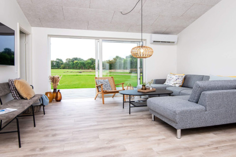 Soggiorno moderno in casa vacanze per 8 persone ad Ansager, Danimarca, con divano grigio e vista sul giardino.