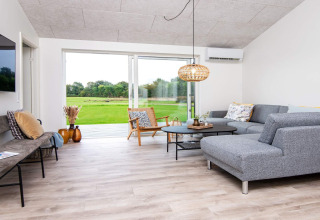 Sala moderna en casa de vacaciones para 8 personas en Ansager, Dinamarca, con sofá gris y grandes ventanales al jardín.
