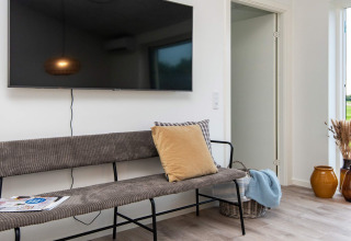 Wohnbereich eines Ferienhauses in Ansager, Dänemark mit Bank, Kissen, TV und braunen Vasen.