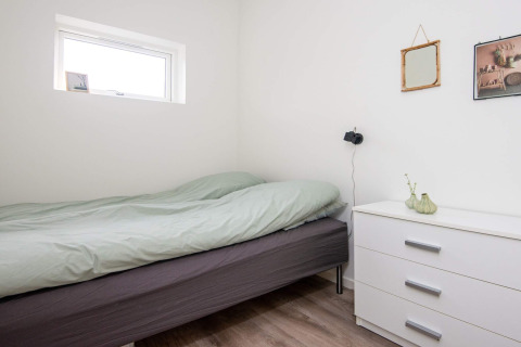 Camera minimalista nella casa vacanze per 8 persone ad Ansager, Danimarca, con letto e cassettiera bianca.