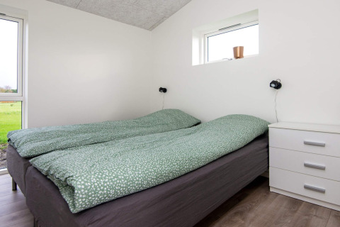 Schlafzimmer mit Doppelbett, grüner Bettdecke, Nachttisch und Fenster im 8-Personen-Ferienhaus in Ansager.