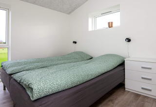 Slaapkamer met tweepersoonsbed, groen dekbed, nachtkastje en raam in 8-persoons vakantiehuis in Ansager.