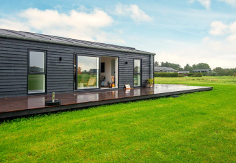 Lodge de vacances moderne à Ansager, Danemark, avec bardage en bois foncé, terrasse et pelouse verte.