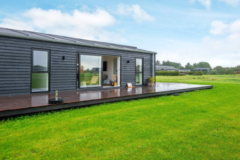 Moderne vakantiewoning in Ansager, Denemarken met donkere houten gevel, groot terras en grasveld.