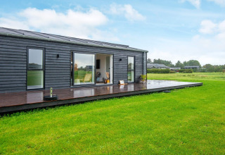 Lodge de vacances moderne à Ansager, Danemark, avec bardage en bois foncé, terrasse et pelouse verte.