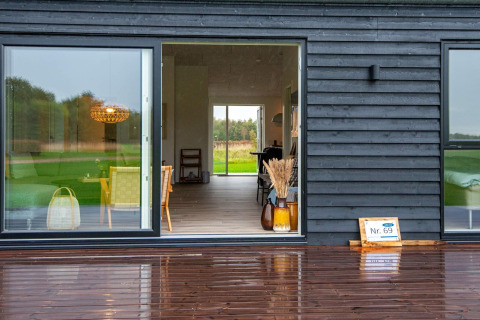 Feriebillede af moderne sort træhytte med stor glasdør, terrasse og naturudsigt i Ansager, Danmark.