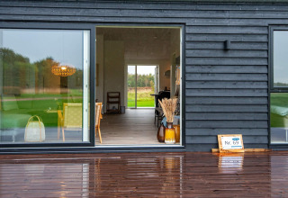Maison de vacances moderne en bois noir avec grande baie vitrée et terrasse mouillée à Ansager, Danemark.