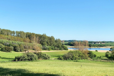 Grüne Landschaft mit See und blauem Himmel beim 12-Personen-Ferienhaus in Millinge, Dänemark.