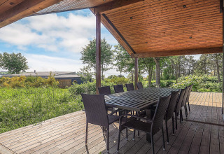 Terrazza coperta in legno con grande tavolo da pranzo e sedie, vista natura presso la casa vacanze a Millinge.