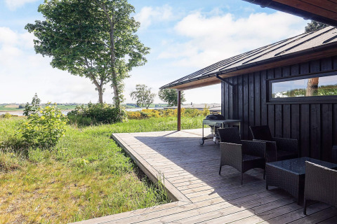 Træterrasse med havemøbler og grill ved 12-personers feriehus i Millinge, Danmark, med udsigt over naturen.