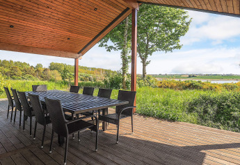 Overdekt houten terras met grote eettafel en stoelen, uitzicht op natuur en meer in Millinge, Denemarken.