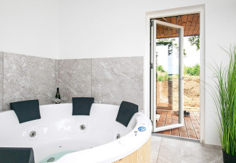 Bubbelbad met vier hoofdsteunen, champagnefles en open deur in vakantiehuis in Millinge, Denemarken.