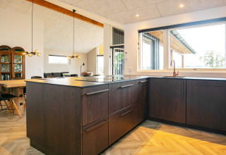 Moderne keuken in een vakantiehuis in Millinge, Denemarken, met donkere kasten en een grote raampartij.