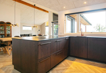 Moderne keuken in een vakantiehuis in Millinge, Denemarken, met donkere kasten en grote ramen.