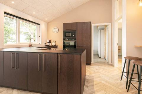 Moderne keuken met donkere houtkasten, groot kookeiland, raam en krukken in Millinge, Denemarken.