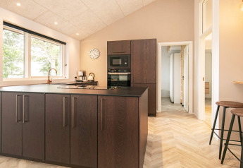 Cocina moderna con gabinetes de madera oscura, isla grande, ventanal y taburetes en Millinge, Dinamarca.