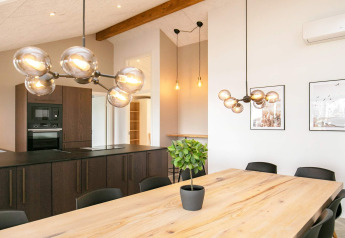 Moderne eet- en keukenruimte in 12-persoons vakantiehuis in Millinge, Denemarken, met houten tafel en lampen.