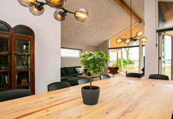 Salle à manger dans maison de vacances à Millinge, Danemark, avec grande table en bois et plante verte.