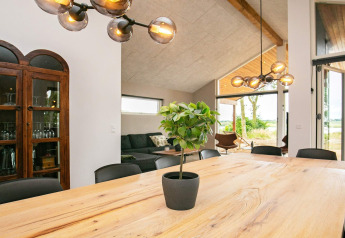 Essbereich im Ferienhaus in Millinge, Dänemark, mit Holz­tisch, Pflanze, Designlampen und Sofa.