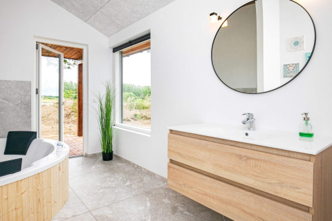 Bagno moderno in una casa vacanze a Millinge, Danimarca, con vasca, mobile in legno e grande specchio tondo.