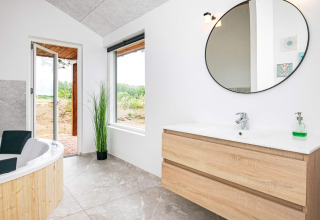 Moderne badeværelse i et feriehus i Millinge, Danmark, med badekar, stor rund spejl og lys indretning.