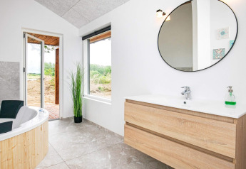 Moderne badkamer in een vakantiehuis in Millinge, Denemarken, met bad, houten meubel en ronde spiegel.