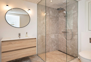 Modern badkamer met inloopdouche, ronde spiegel en houten wastafel in een vakantiehuis in Millinge, Denemarken.