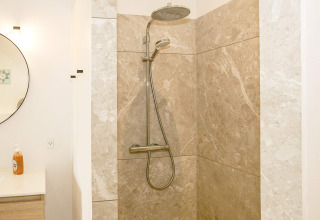 Moderne douche met regendouche en beige marmeren tegels in 12-persoons vakantiewoning in Millinge, Denemarken.