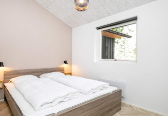 Slaapkamer met tweepersoonsbed, witte dekbedden en raam in 12-persoons vakantiehuis in Millinge, Denemarken.