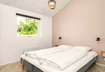 Chambre avec lit double, murs clairs, fenêtre vue nature dans la location de vacances à Millinge, Danemark.