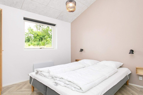 Slaapkamer met dubbel bed, lichte muren, raam met natuurzicht in vakantieverblijf Millinge, Denemarken.
