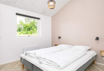Slaapkamer met tweepersoonsbed, lichte muren en raam met natuurzicht in vakantiehuis Millinge, Denemarken.