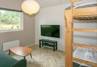 Salon avec lit superposé, table basse, TV écran plat et vue nature dans une maison de vacances à Millinge.