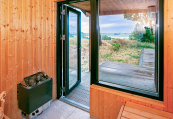 Vue depuis le sauna en bois avec porte ouverte sur terrasse et paysage à Millinge, Danemark.