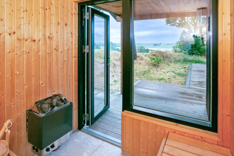 Uitzicht vanuit houten sauna met open deur naar terras en landschap in Millinge, Denemarken.