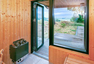 Uitzicht vanuit houten sauna met open deur naar terras en landschap in Millinge, Denemarken.
