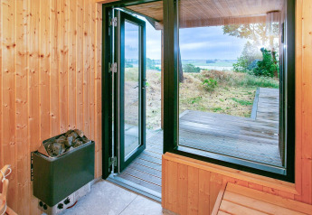 Uitzicht vanuit houten sauna met open deur naar terras en landschap in Millinge, Denemarken.