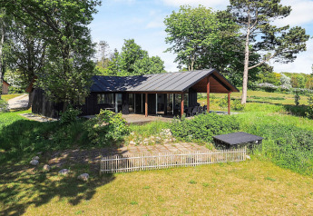 Moderne vakantiehuis in Millinge, Denemarken, omgeven door groen met overdekt terras en tuin.