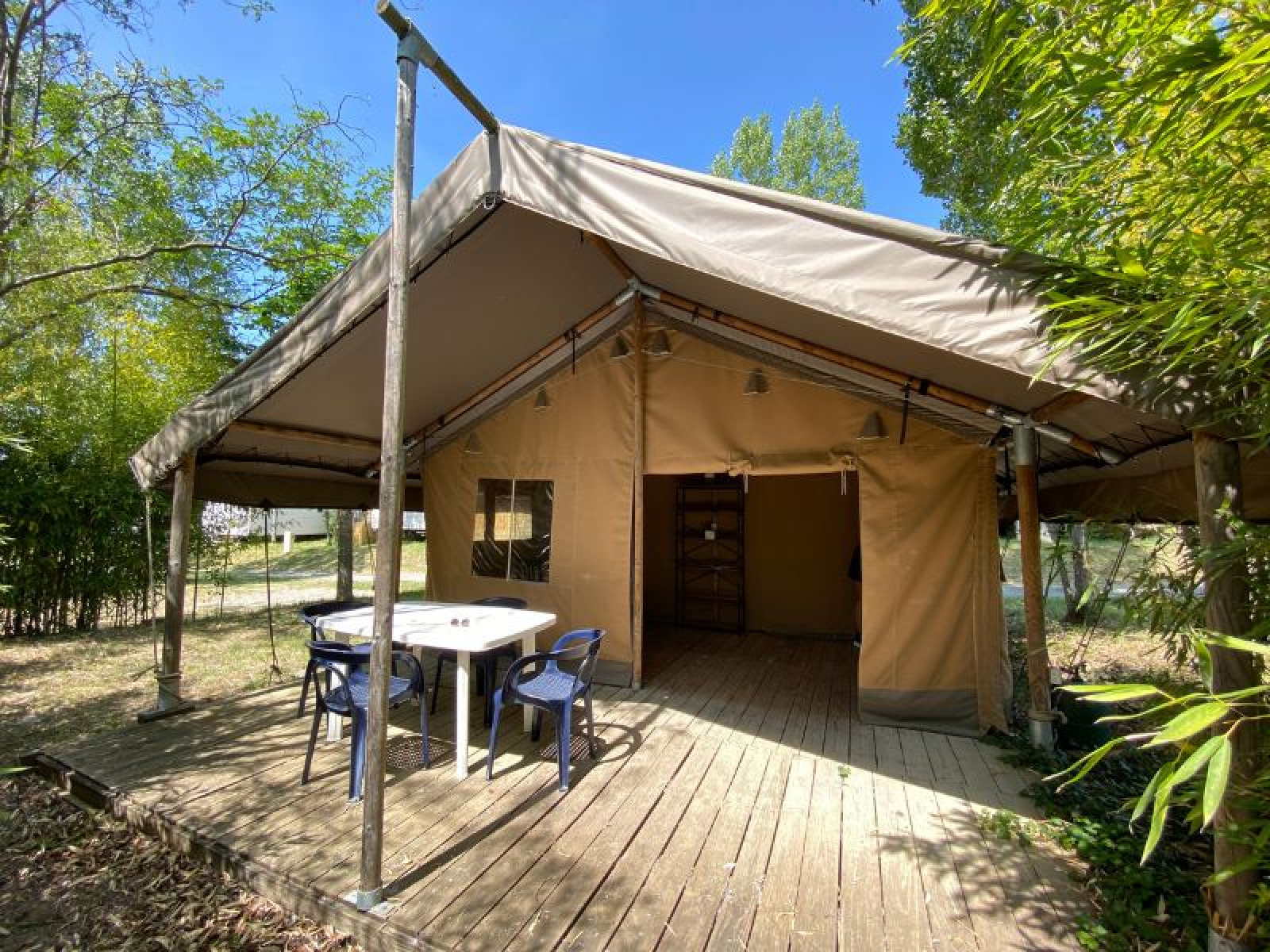 Safaritent Lodge COSY met houten vlonder, zitje en tafel, omgeven door bomen en groene natuur.